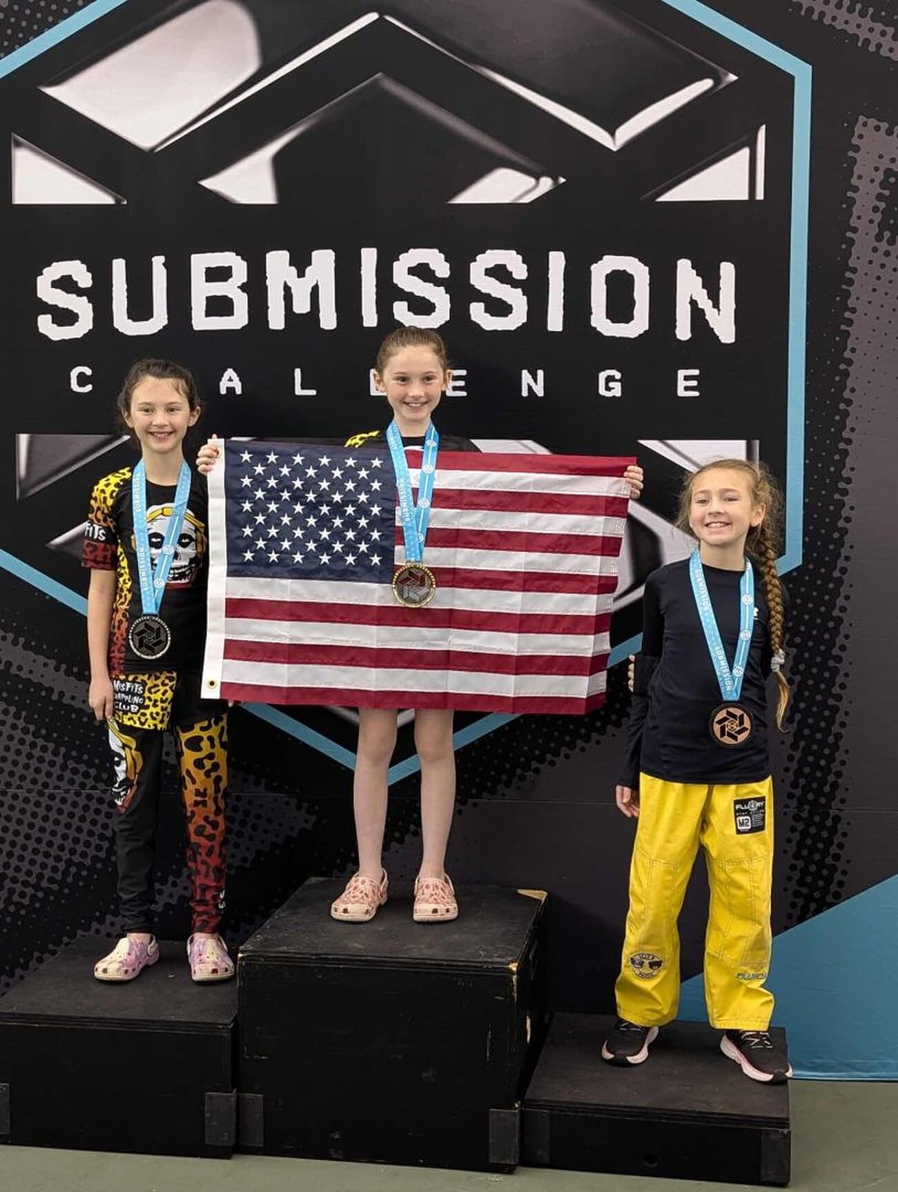 Three young Misfits grapplers on a Submission Challenge podium with medals