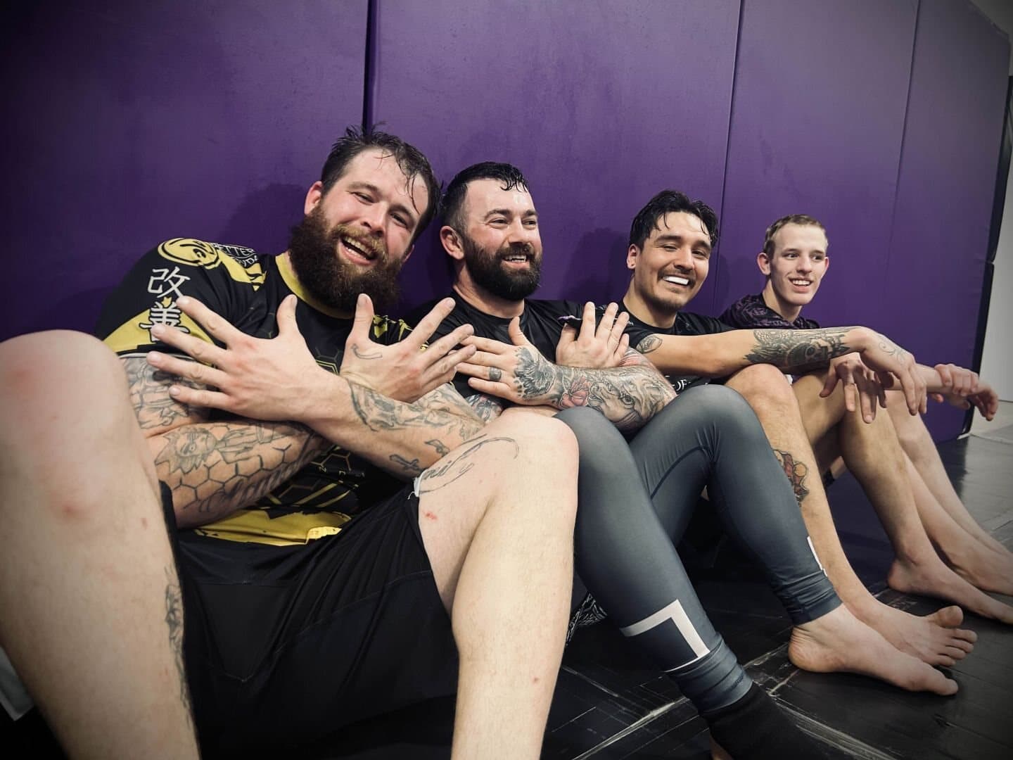Four Misfits teammates against the purple mat wall throwing the crossed-arm X